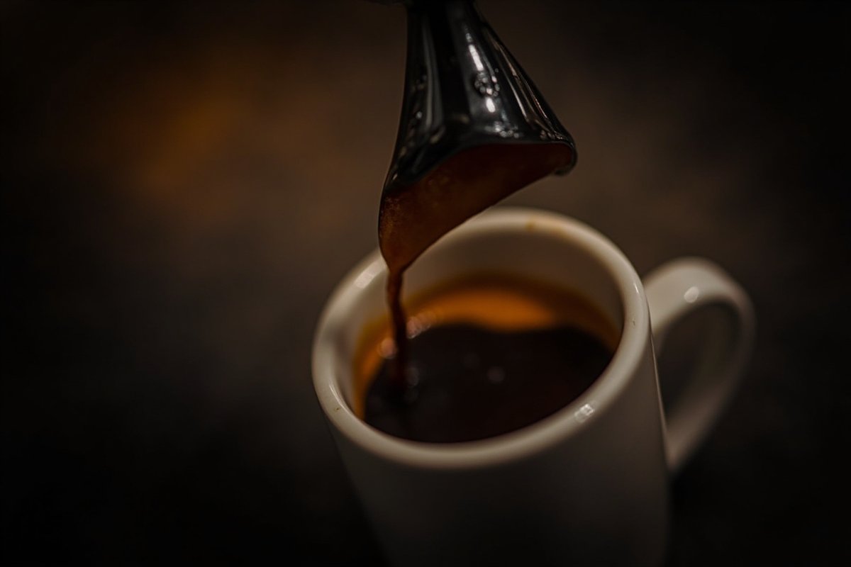 濃縮咖啡從濾杯滴落到白瓷杯中,金黃色 crema 在深色咖啡液上形成